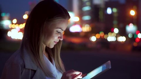 Attractive girl reading on the tablet great news, happy against the night road.