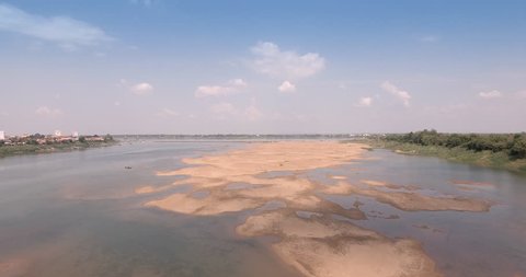 Retreating drone shot of sandbanks in Mekong river during dry season. Bridge and town as backdrop 