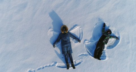 Mom and son make snow angels together. Camera slowly rising. Aerial footage.