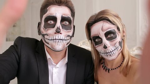 Portrait of scary people with a terrible makeup in the form of a skull or dead people. Couple very scared laughing showing teeth. Outfit for halloween. A couple of zombies take selfies on Halloween.