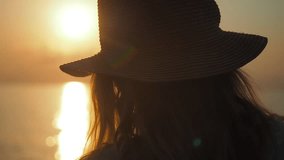 Young woman in a straw hat relaxing, looking at sea during sunset. Lifestyle video, people in nature concept. 