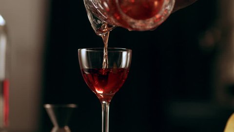 Classic bartender pouring liquor from a tall glass to a cocktail glass in interior classy bar with soft interior lighting. Close up shot on 4k RED camera.