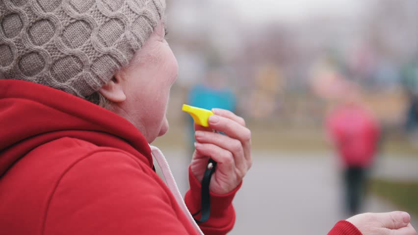 An old woman blows on whistle amd two elderly women starts walking on sticks of nordic walking