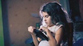 little girl in the evening reads social media posts on a tablet in the room indoors. children and lifestyle internet concept