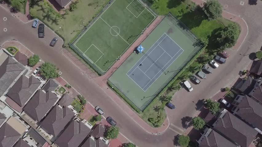 An aerial view of houses of a gated community un Guayaquil, Ecuador. Shot with a drone in a sunny day looking straight down to a playground with a tennis court, a pool and a soccer field.