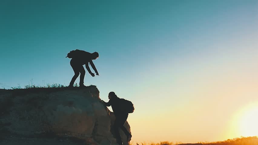 Silhouette of helping hand between two climber. two hikers on top of the mountain, a man helps a man to climb a sheer stone. couple hiking help each other silhouette in mountains with sunlight. Royalty-Free Stock Footage #1019381923