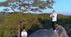 two musicians standing on a rock in white shirts and playing on the trumpet aerial 4k 50p