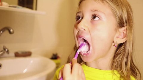 Little child girl face portrait brushing her teeth with a toothbrush in bathroom in the morning