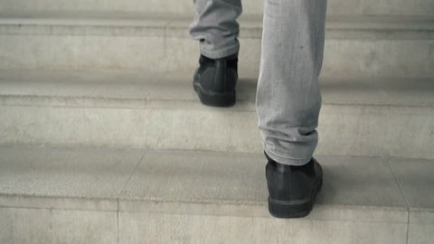 Rear view of unrecognizable man legs wearing gray jeans and black boots going upstairs. Tracking slow motion medium shot