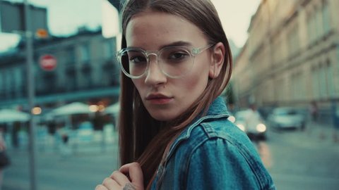 Portrait young woman with glasses look at camera poses in city center beautiful hair attractive smile girl lady jacket lifestyle summer close up face slow motion