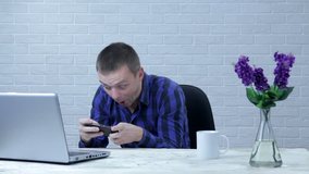 Funny scared young man playing mobile game with shocked face at office