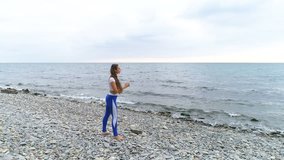 Girl is doing exercise for legs the bodyflex during breathing exercises on the sea and rock background. Aerial video.
