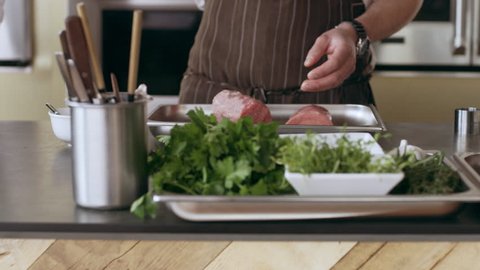 Chef placing pieces of veal onto a tray and salting them in interior kitchen with soft day lighting. Close up shot on 4k RED camera.