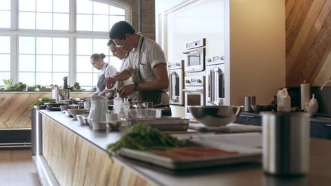 Three professional chefs cooking and preparing food on a large countertop, in interior kitchen with soft day lighting. Medium shot on 4k RED camera.