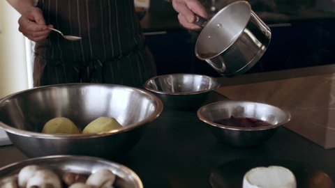 Chef taking a pot of hot, steaming water into another bowl and carries the bowls to his work station in interior kitchen with soft day lighting. Medium shot on 4k RED camera.