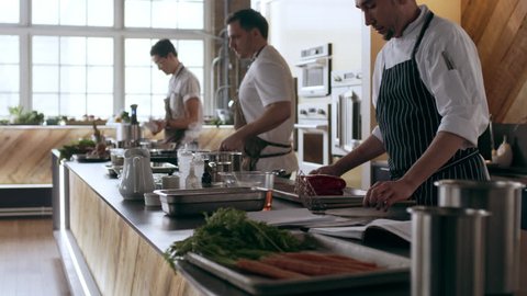 Chefs walking into kitchen to start cooking at station in interior kitchen with soft day lighting. Wide to Close up shot on 4k RED camera.