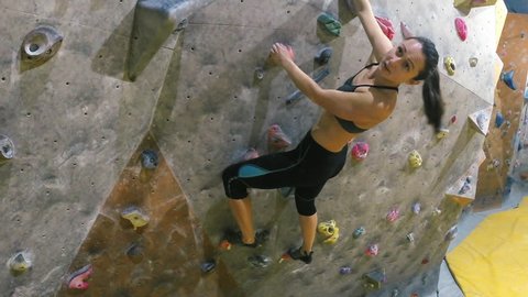 Young sporty woman on climbing wall indoor bouldering to the top