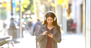 Front view of a happy teen walking towards camera listening to music in the street