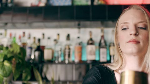 Serious and proficient barmaid, shaking a cocktail shaker in the air in a fancy bar with soft interior lighting. Close up shot on 4k RED camera.