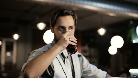 Brunette jew man drinking a dark beer in a bar.