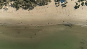Aerial top view of sand beach with small waves and walking people.