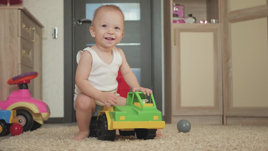 Lovely baby boy playing with a big car toy on floor at home. Kid boy toddler playing with toy car indoors. Future driver. Funny toddler boy indoors.