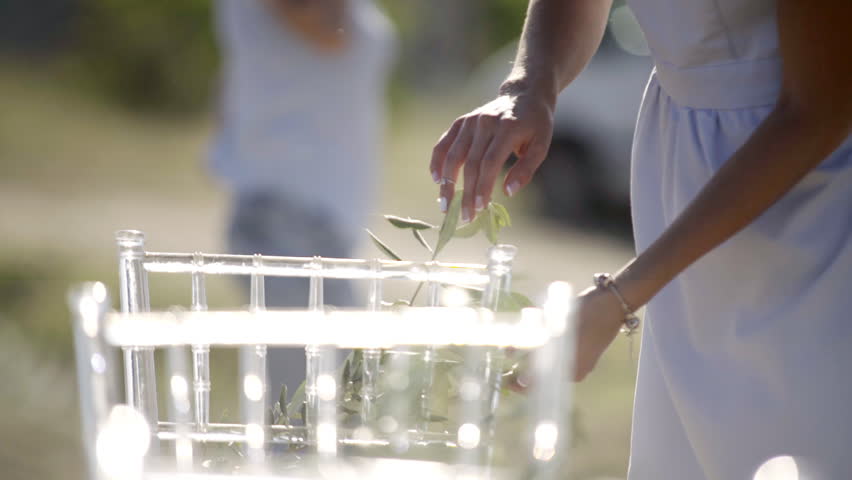 Crop unrecognizable woman in white gown decorating plastic chairs for wedding in Crimea 