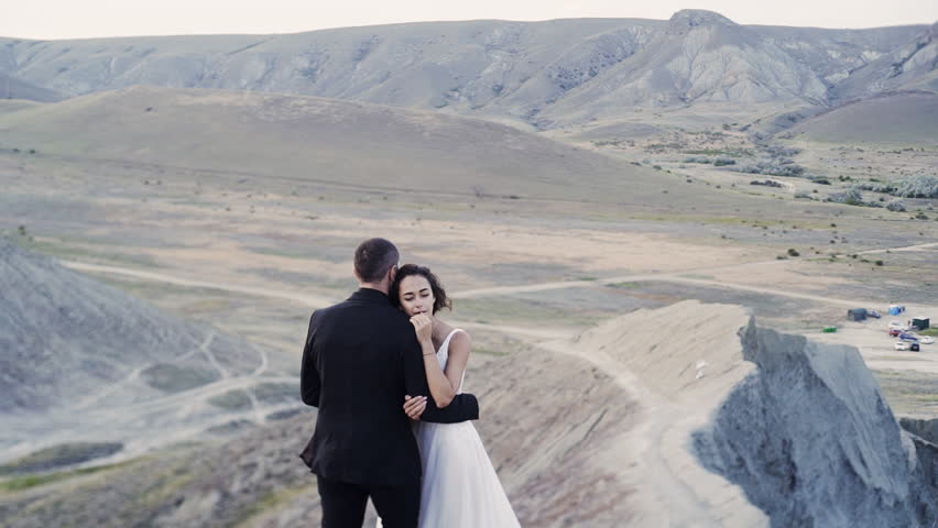 Motion around of newlywed couple embracing on high top hill over beautifu landscape. Crimea, Chameleon cape, Koktebel