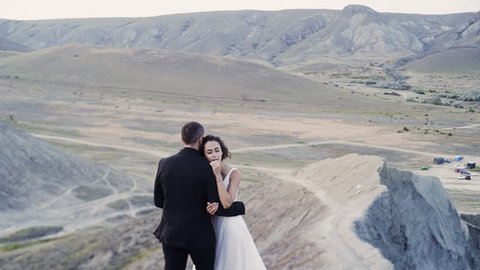 Motion around of newlywed couple embracing on high top hill over beautifu landscape. Crimea, Chameleon cape, Koktebel