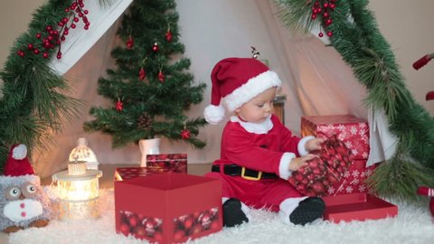 Adorable little toddler baby boy dressed in canta claus costume, playing at home in front of teepee decorated for Christmas
