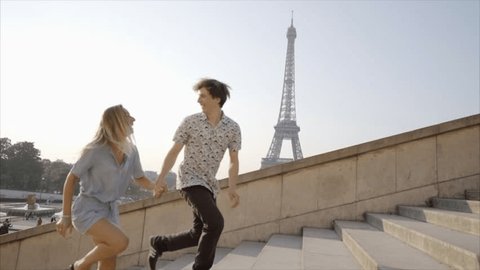 Young couple having fun running up the stairs at the Tour Eiffel in Paris, France. Two people laughing, boyfriend holding girlfriends hand pulling her up. City trip vacations 