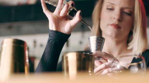 Skillful female bartender pouring shots of alcohol into a cocktail shaker in a fancy bar with soft interior lighting. Close up shot on 4k RED camera.