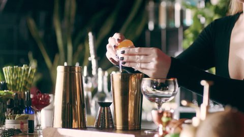 Skillful female bartender cracking an egg and separating the egg yolk from the whites over a cocktail shaker in a fancy bar with soft interior lighting. Close up shot on 4k RED camera.