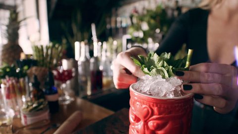 Tiki cocktail glass being decorated with little umbrella by barmaid in interior fancy bar with soft day lighting. Close up shot on 4k RED camera.