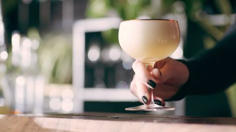 Young professional barmaid spraying a perfume spray over a bourbon sour cocktail and serving it in a fancy bar with soft interior lighting. Close up shot on 4k RED camera.