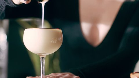 Cocktail poured in a glass by a proficient female mixologist on a counter in a fancy bar with soft interior lighting. Close up shot on 4k RED camera on a gimbal.