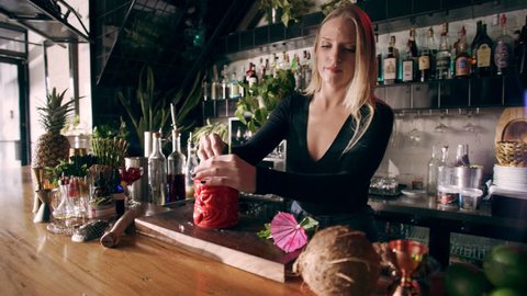 Close up of professional female mixologist garnishing drink with straw and herbs in interior fancy bar with soft day lighting. Close up to Medium shot on 4k RED camera on a gimbal.