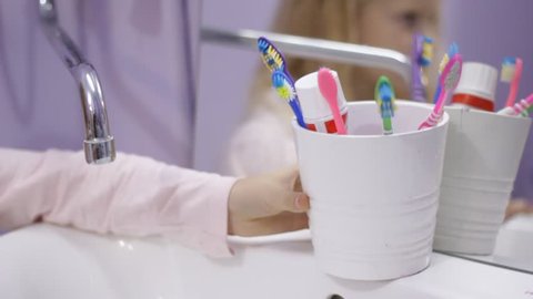 Happy blonde child kid girl laughing and girl puting a toothbrush in a cup for brushes. Health care, dental hygiene, people and beauty concept