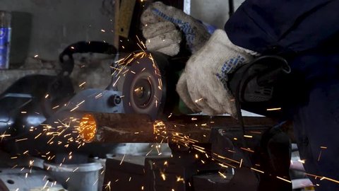 Male hand cuts off pieces of water pipe with angle grinder. Cutting of a steel with splashes of sparks at construction site. Sparks during cutting of metal angle grinder