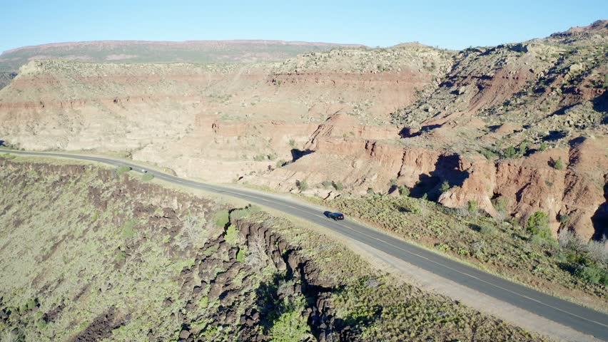 Aerial tracking of a Jeep Grand Cherokee driving along a road on top of a rocky ridge, in the southwestern desert landscape of Utah.