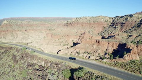 Aerial tracking of a Jeep Grand Cherokee driving along a road on top of a rocky ridge, in the southwestern desert landscape of Utah.