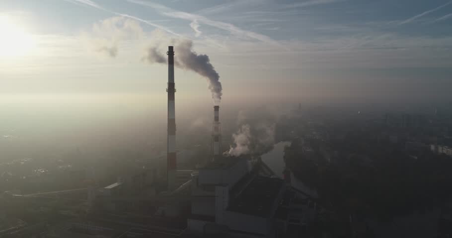 Aerial view of smoking chimneys of CHP plant and smog over the city and builidings in the background - Wroclaw, Poland