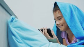 Portrait of cute girl under blanket with smartphone. little girl playing online games under a social media blanket. girl and smartphone lifestyle under the covers concept