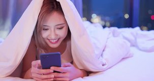 woman use smart phone happily and lying down on the bed under quilt at night