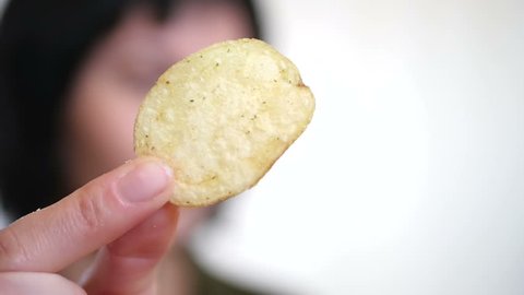 Girl brunette eats potato chips on a white background, close-up. Woman holds chips in hand close-up, then puts in her mouth.