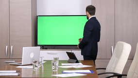 Businessman in conference room pointing to a green screen mock-up TV. Dolly slider 4K footage