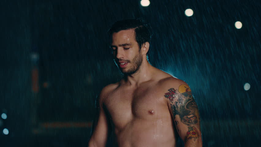 Shirtless Athletic Muscular Young Man is Celebrating His Sport Accomplishments on a Rainy Night. He is in an Urban Environment Under a Brindge with Cars in the Background.