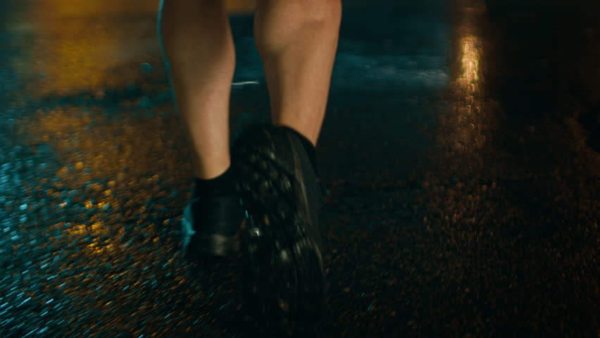 Close Up Leg Shot of an Athletic Young Man in Sports Outfit Jogging in a Rainy Street. He is Running in a Dark Urban Environment Under a Brindge with Cars in the Background.