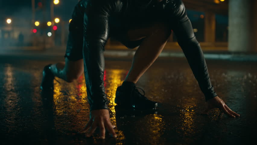 Strong Muscular Fit Young Man Starts Sprinting on a Rainy Evening. He is Running in an Urban Environment Under a Bridge with Cars in the Background.