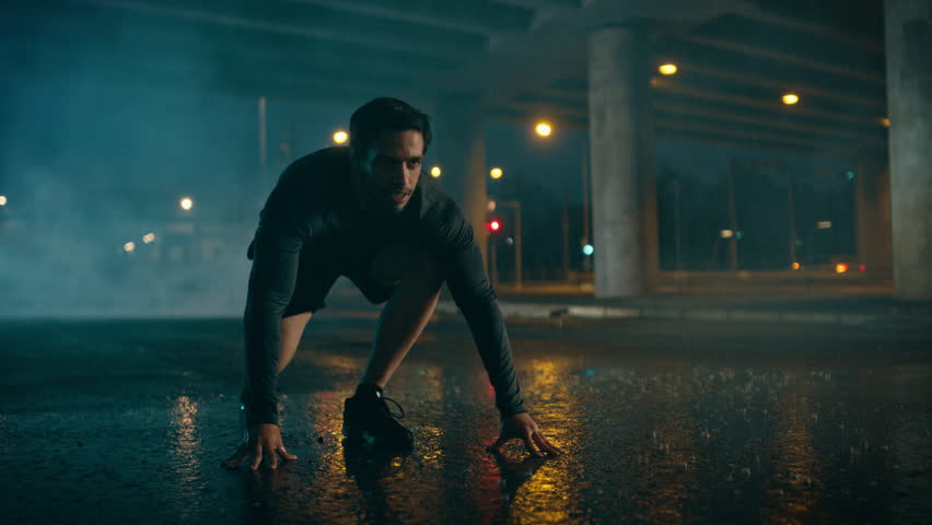 Strong Muscular Fit Young Man Starts Sprinting on a Rainy Evening. He is Running in an Urban Environment Under a Bridge with Cars in the Background.